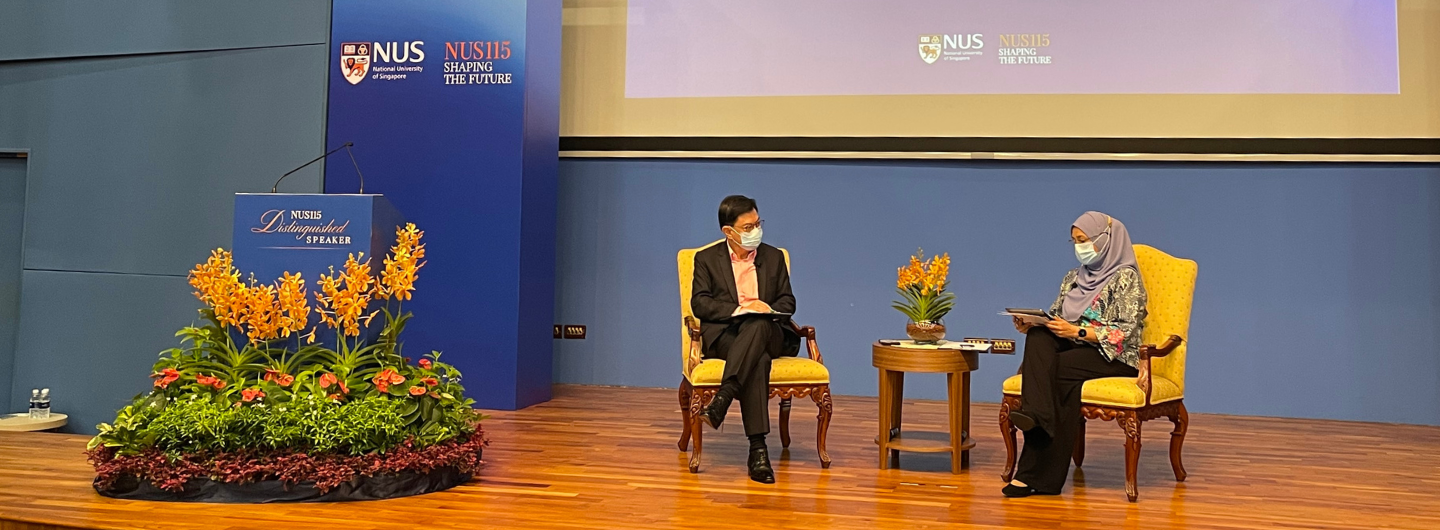 NUS Distinguished Speaker event with two seated speakers wearing masks on stage.